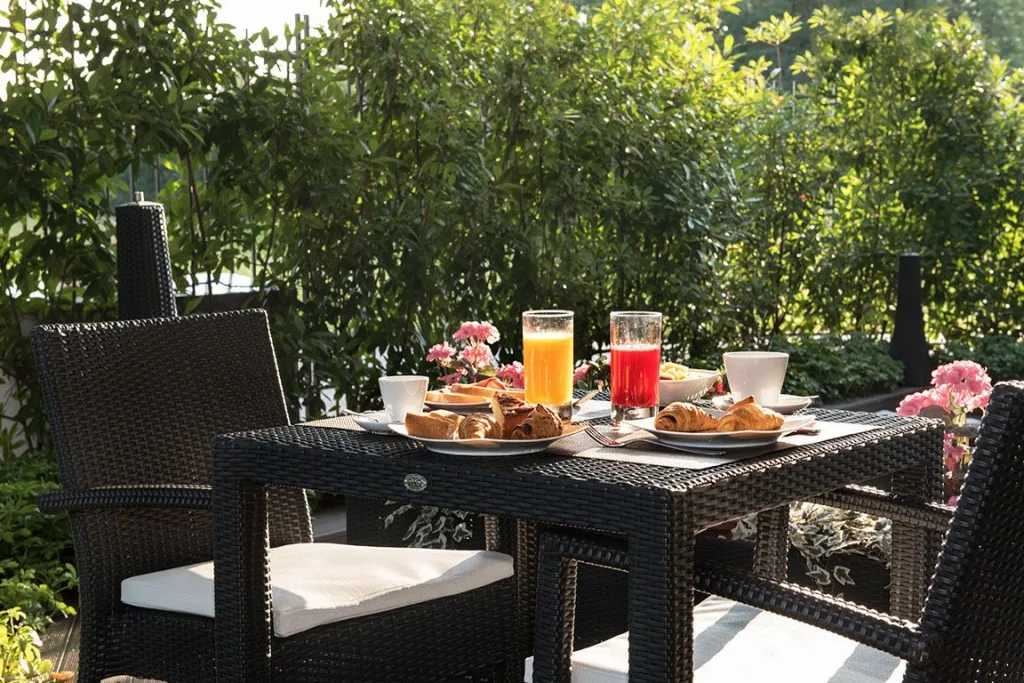 Espacio representativo del hotel: Mesa de comedor al aire libre con desayuno junto a un jardín frondoso.