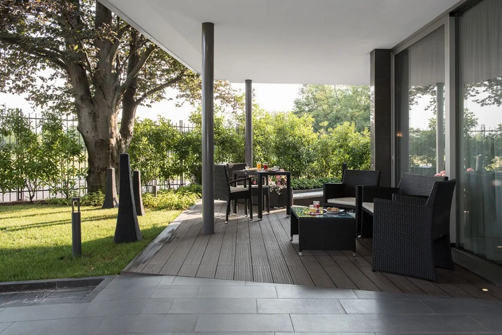 Espacio representativo del hotel: Un patio exterior cubierto con asientos y una mesa da a un jardín.