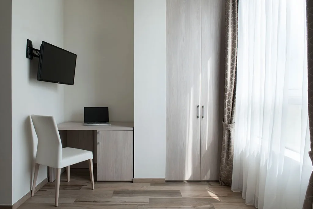Espacio representativo del hotel: Un rincón de dormitorio con escritorio, silla y televisor montado en la pared.