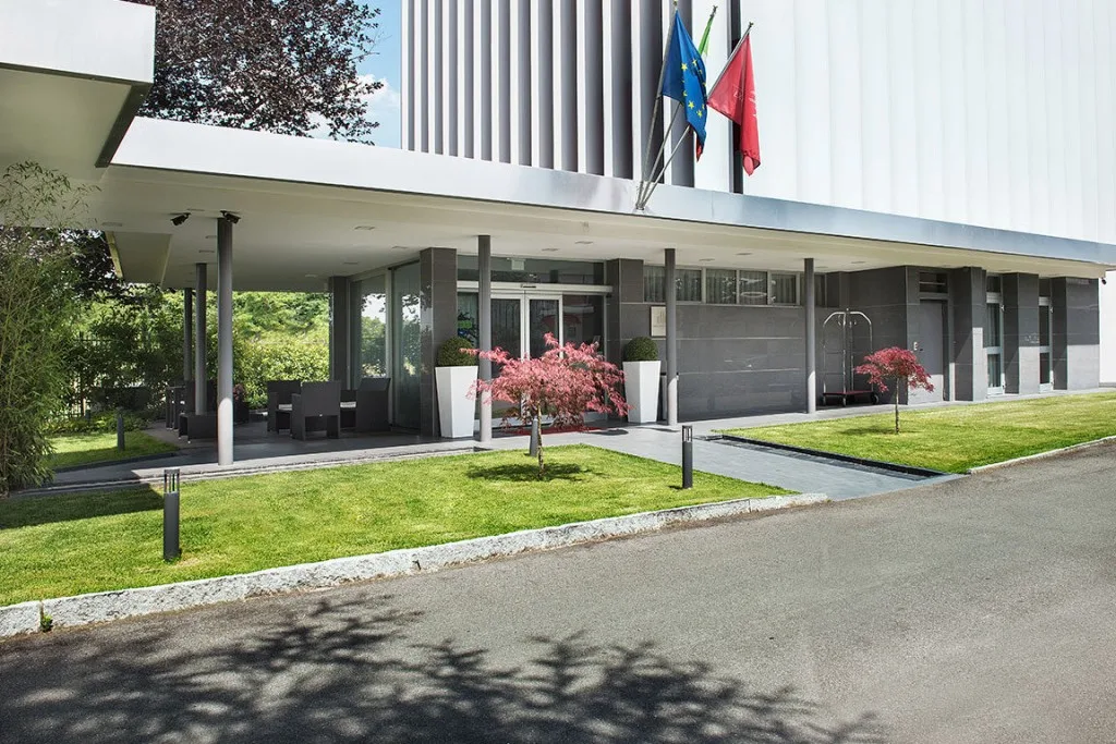 Espacio representativo del hotel: La entrada de un edificio moderno da a una vía pavimentada, con jardines y banderas.