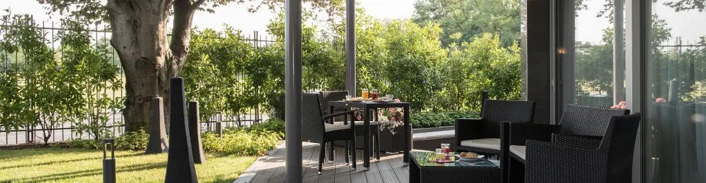 Espacio representativo del hotel: Una zona de estar al aire libre junto a grandes ventanales da a un jardín frondoso.