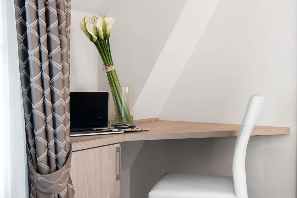 Espacio representativo del hotel: Un escritorio con una computadora portátil y flores está junto a una cortina estampada.