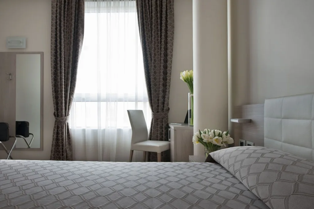 Espacio representativo del hotel: Dormitorio con una cama grande, una silla y una ventana luminosa con cortinas.