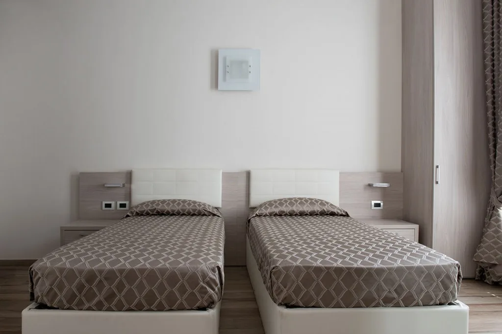 Espacio representativo del hotel: Un dormitorio con dos camas individuales bajo un panel de control en la pared.