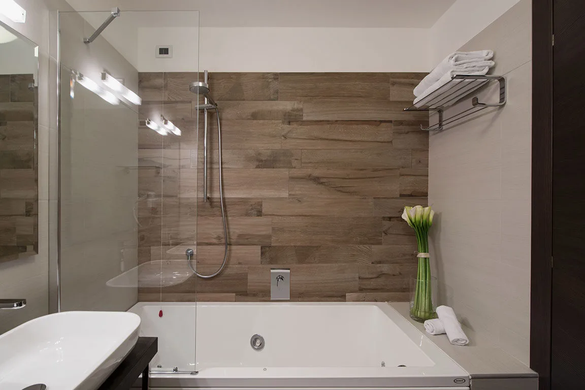 Espacio representativo del hotel: Un baño con bañera, mampara de vidrio y paredes revestidas de azulejos.