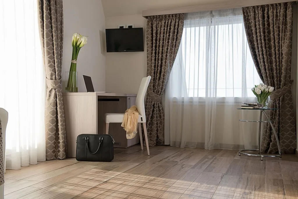Espacio representativo del hotel: Habitación de hotel con escritorio, asiento y grandes ventanas con cortinas.