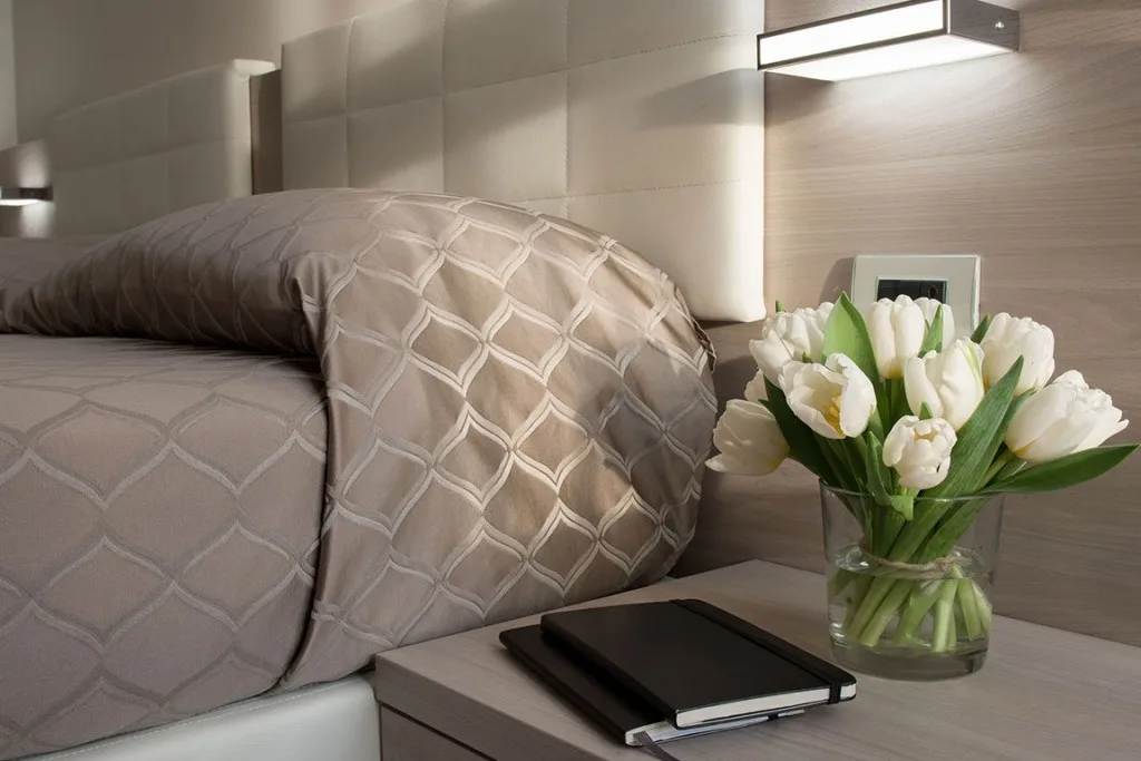 Espacio representativo del hotel: Una cama tendida con ropa de cama estampada y un jarrón de flores al lado.