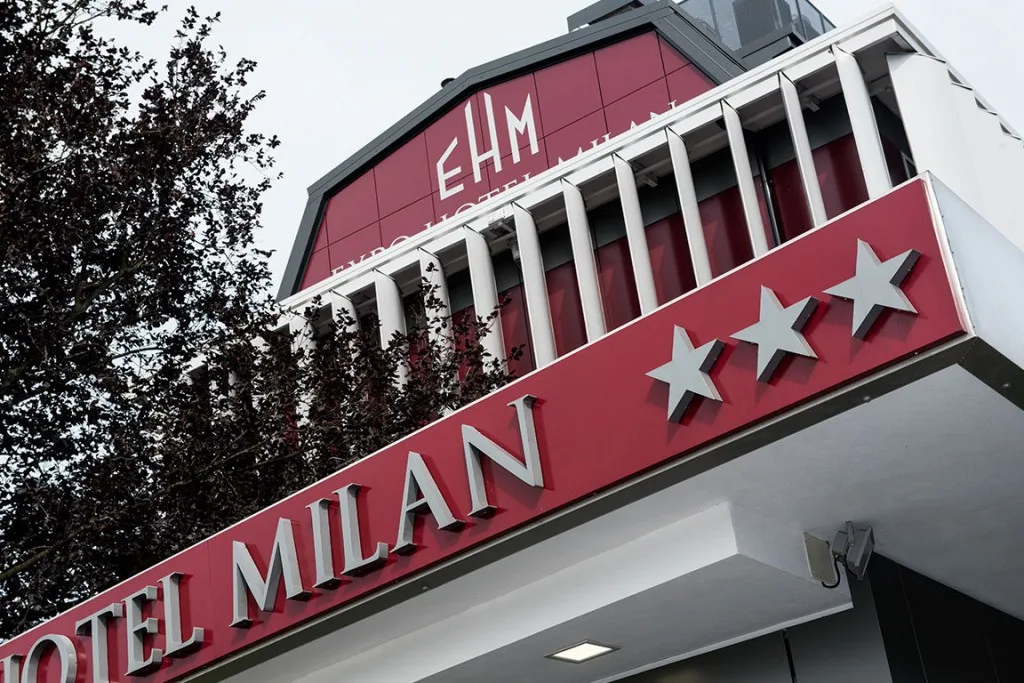 Espacio representativo del hotel: Una fachada roja de hotel muestra el nombre Milan y tres símbolos de estrellas.