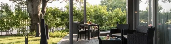 Espacio representativo del hotel: Zona de asientos al aire libre junto a grandes ventanales, con una mesa y vegetación.