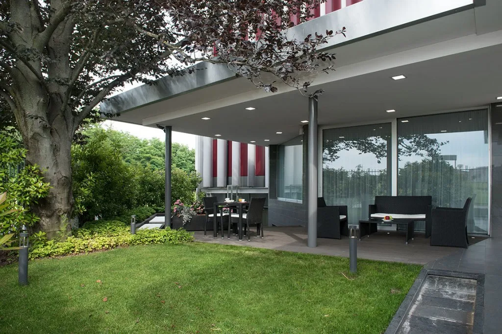 Espacio representativo del hotel: Un patio cubierto con asientos al aire libre junto a un césped y puertas de vidrio.