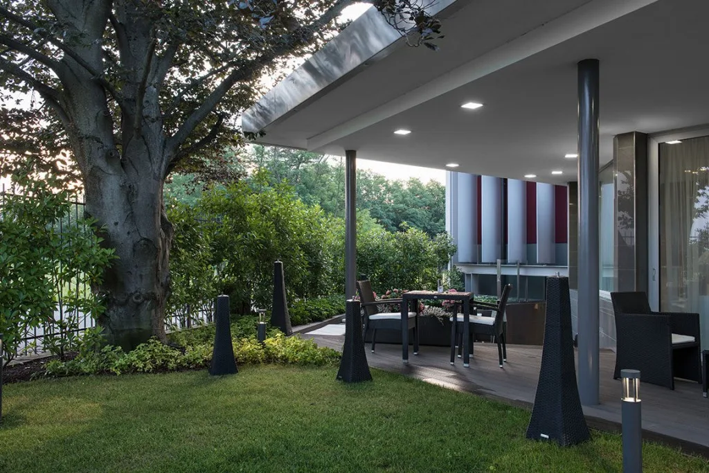Espacio representativo del hotel: Una zona de comedor exterior cubierta da a un jardín con árboles y arbustos.