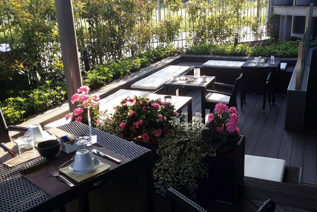 Espacio representativo del hotel: Una terraza de comedor al aire libre con mesas junto a jardineras con flores.