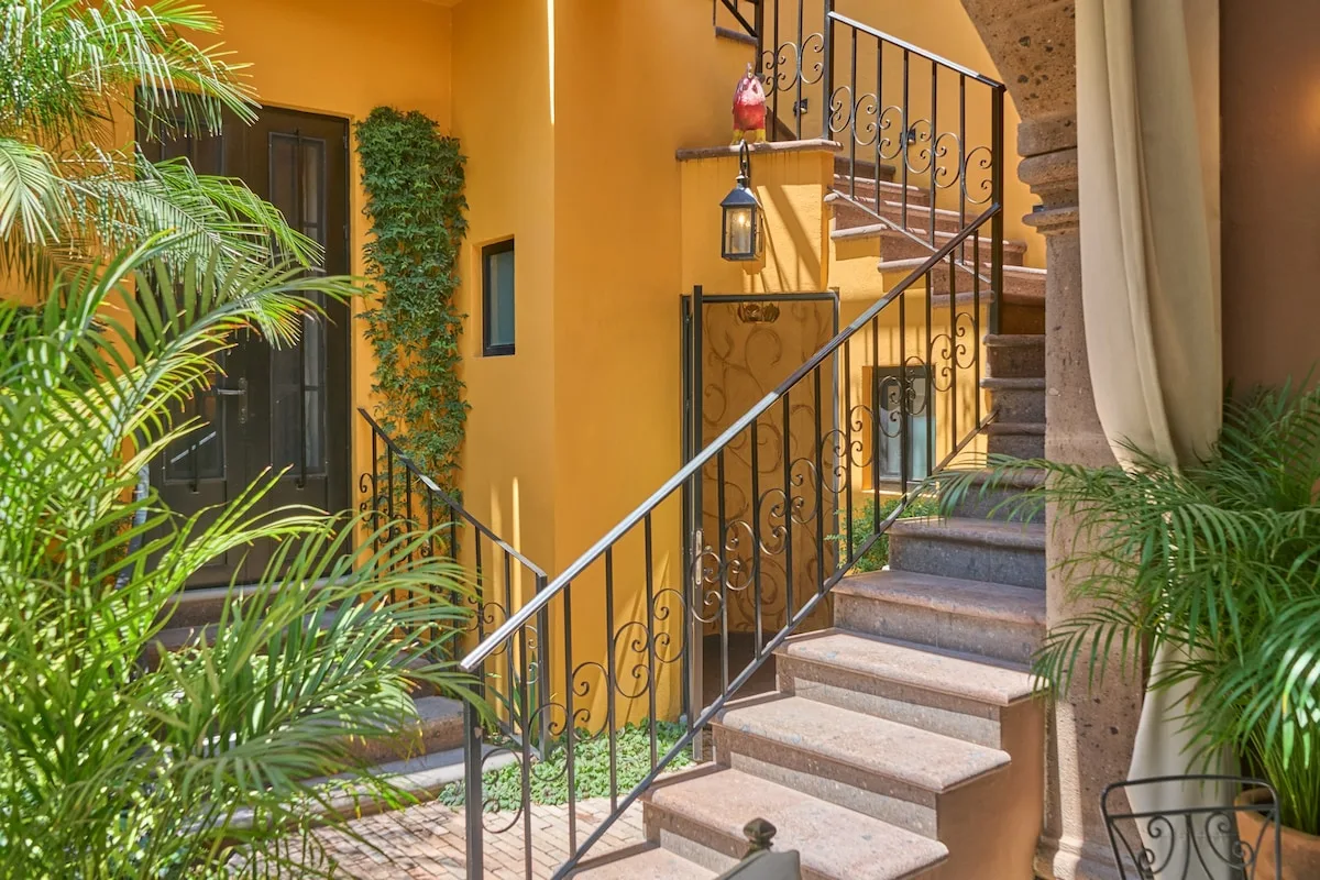 Una escalera exterior con barandilla metálica negra junto a un edificio de color ocre.