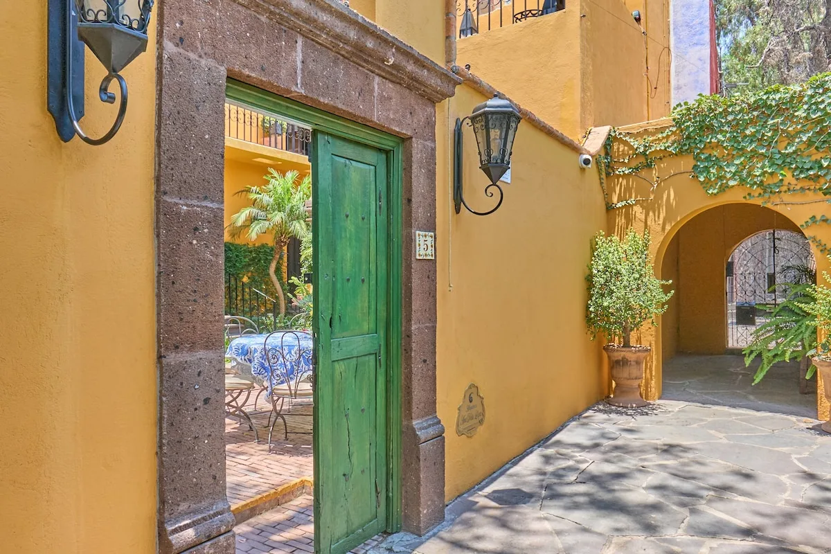 La entrada de un patio amarillo tiene una puerta verde y un arco cubierto de hiedra.