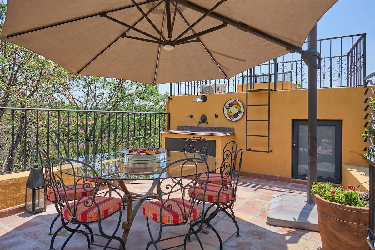 Un patio al aire libre tiene una mesa de comedor bajo una sombrilla grande.
