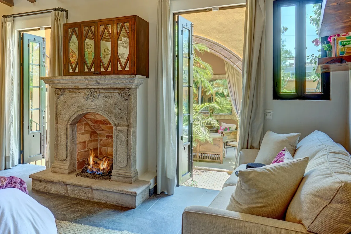 Una sala luminosa con chimenea de piedra y asientos junto a puertas abiertas.