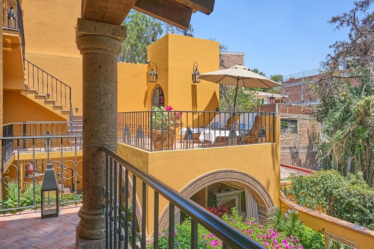 Una terraza exterior con mesa y sillas está sobre un pasadizo arqueado.