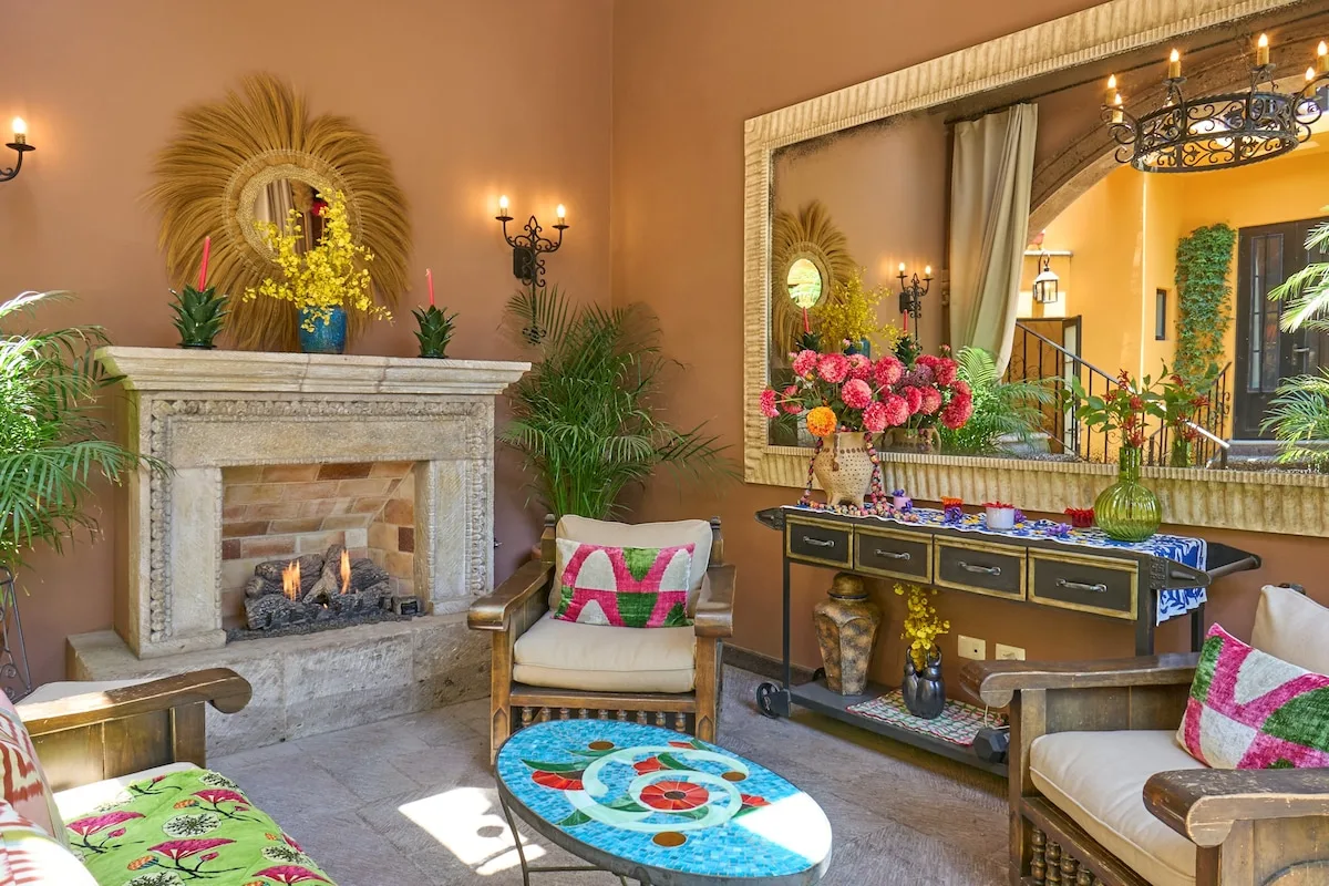 A warm-toned living room features a fireplace, seating, and a console beneath a large mirror.