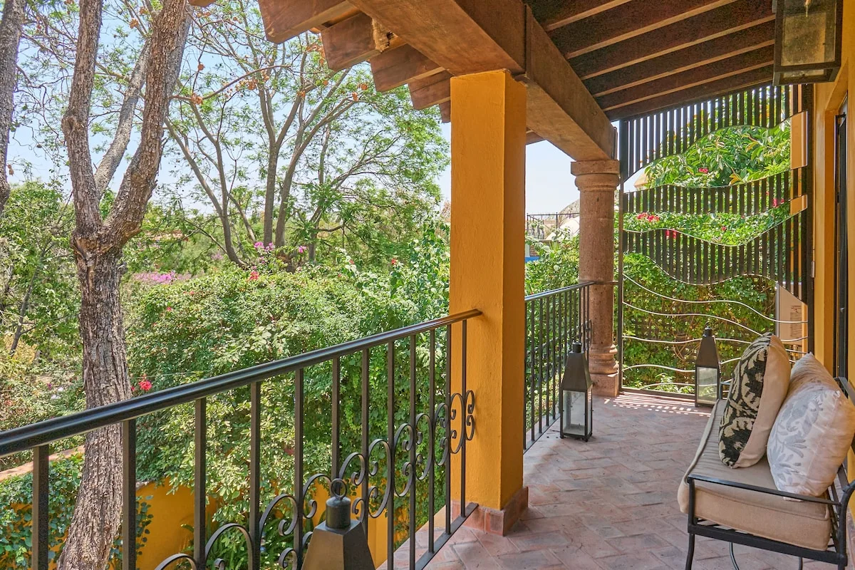 Un patio exterior cubierto tiene una barandilla, asientos y vistas a la vegetación.