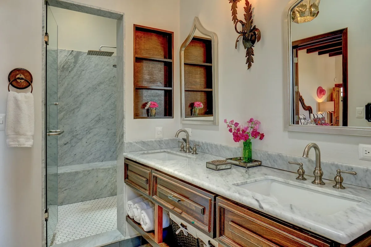 Un lavabo de baño con encimera de mármol está junto a una ducha con mampara de vidrio.