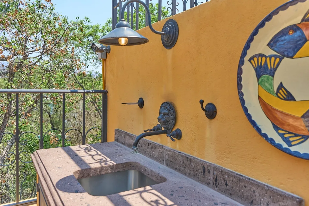 Un lavabo exterior junto a un mural decorativo de un ave en una pared ocre.