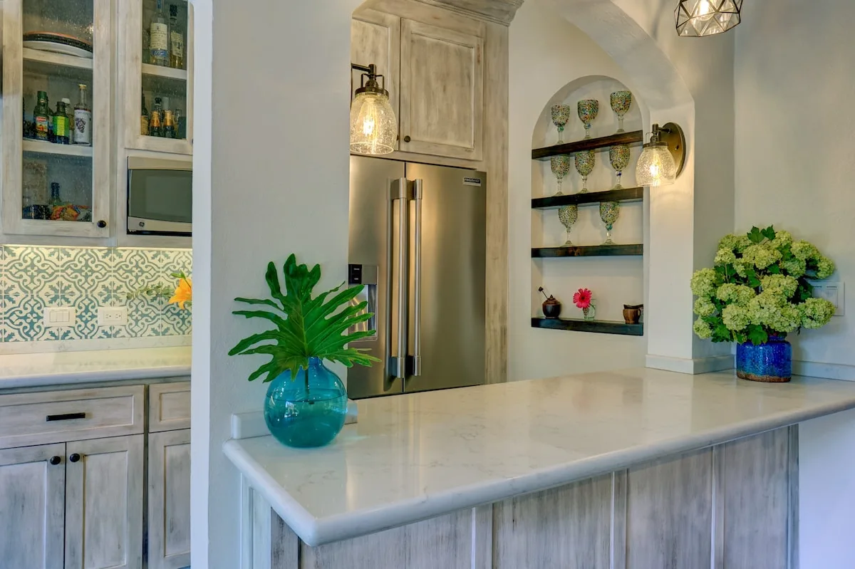 Una cocina luminosa con una isla grande, un refrigerador de acero inoxidable y estantes empotrados.