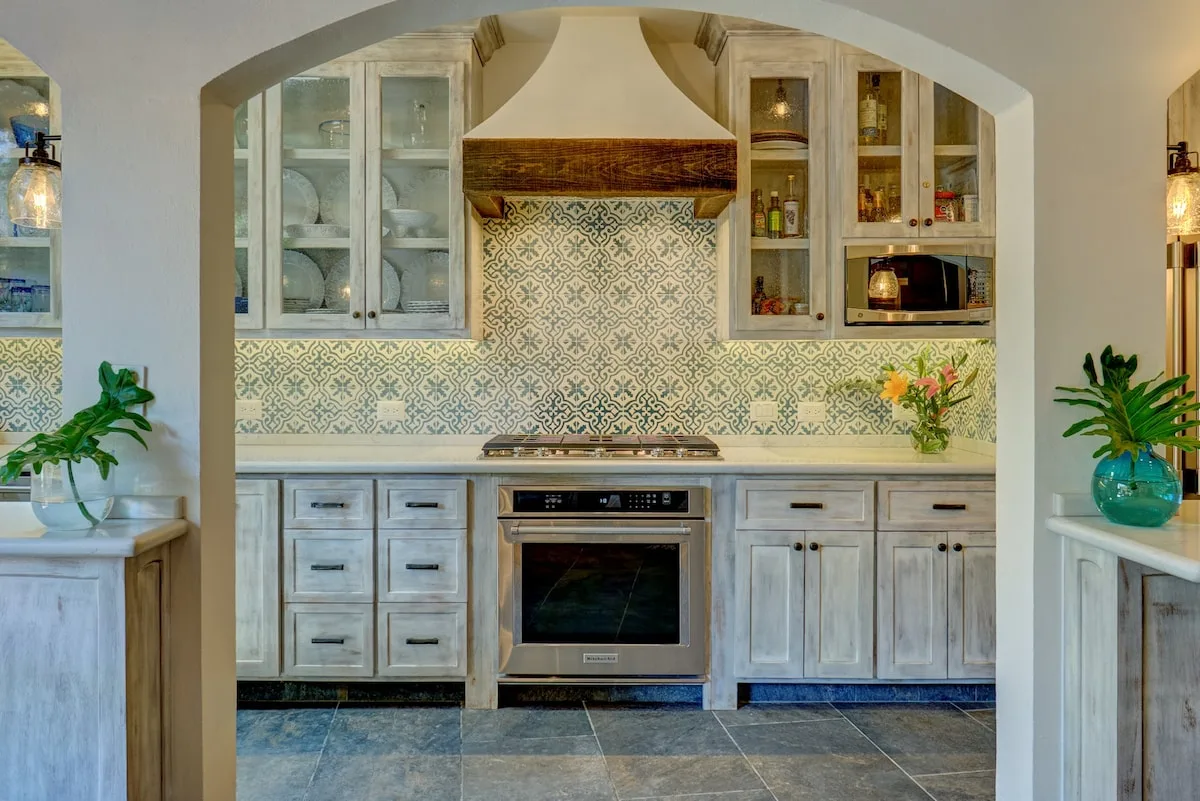 Una cocina con gabinetes claros, azulejos estampados y una estufa central.
