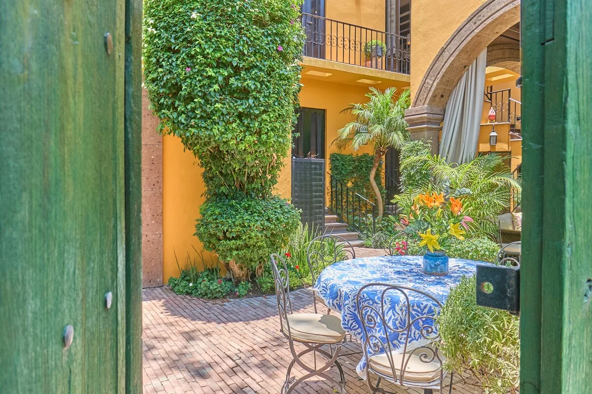 Un comedor en un patio con un mantel azul estampado y vegetación alrededor.