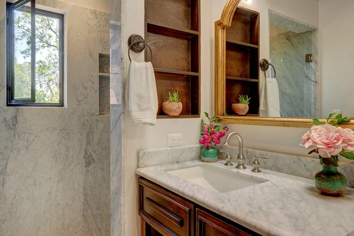 Un baño de mármol con lavabo, espejo de pared y ducha de vidrio.