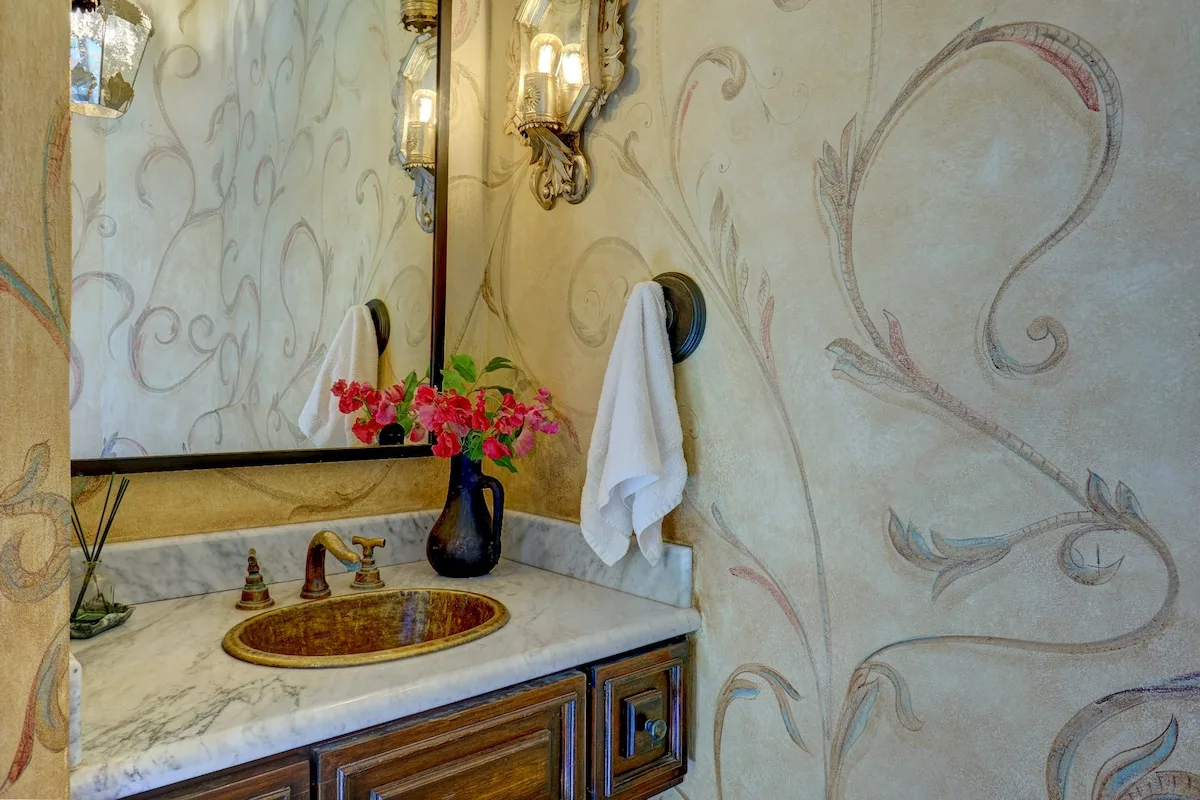 Un tocador de baño decorado con lavabo, motivos florales en la pared y una toalla.