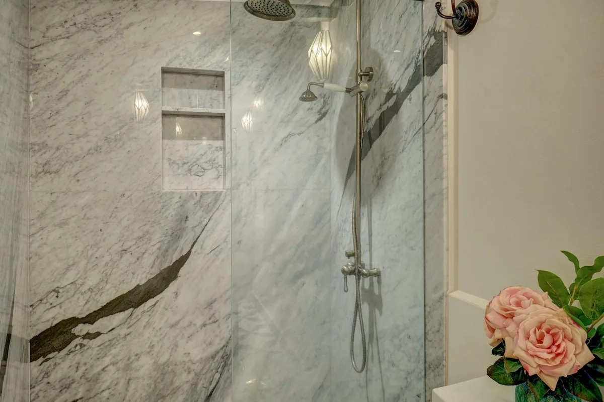 Una ducha con azulejos de mármol, un nicho en la pared y accesorios montados.