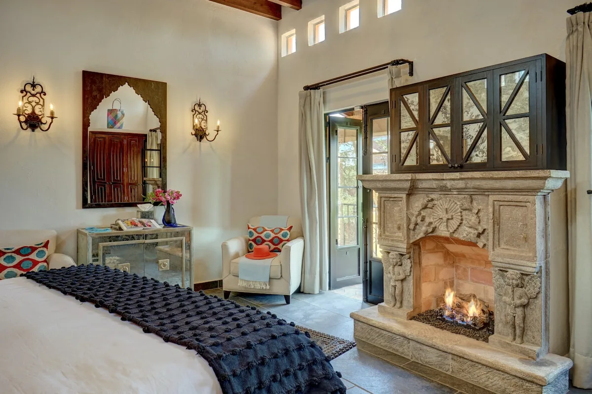 Un dormitorio con una cama y una chimenea de piedra junto a ventanas altas.