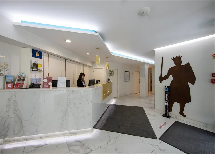 Espacio representativo del hotel: Una recepción de hotel con una persona detrás del mostrador y una alfombra oscura.