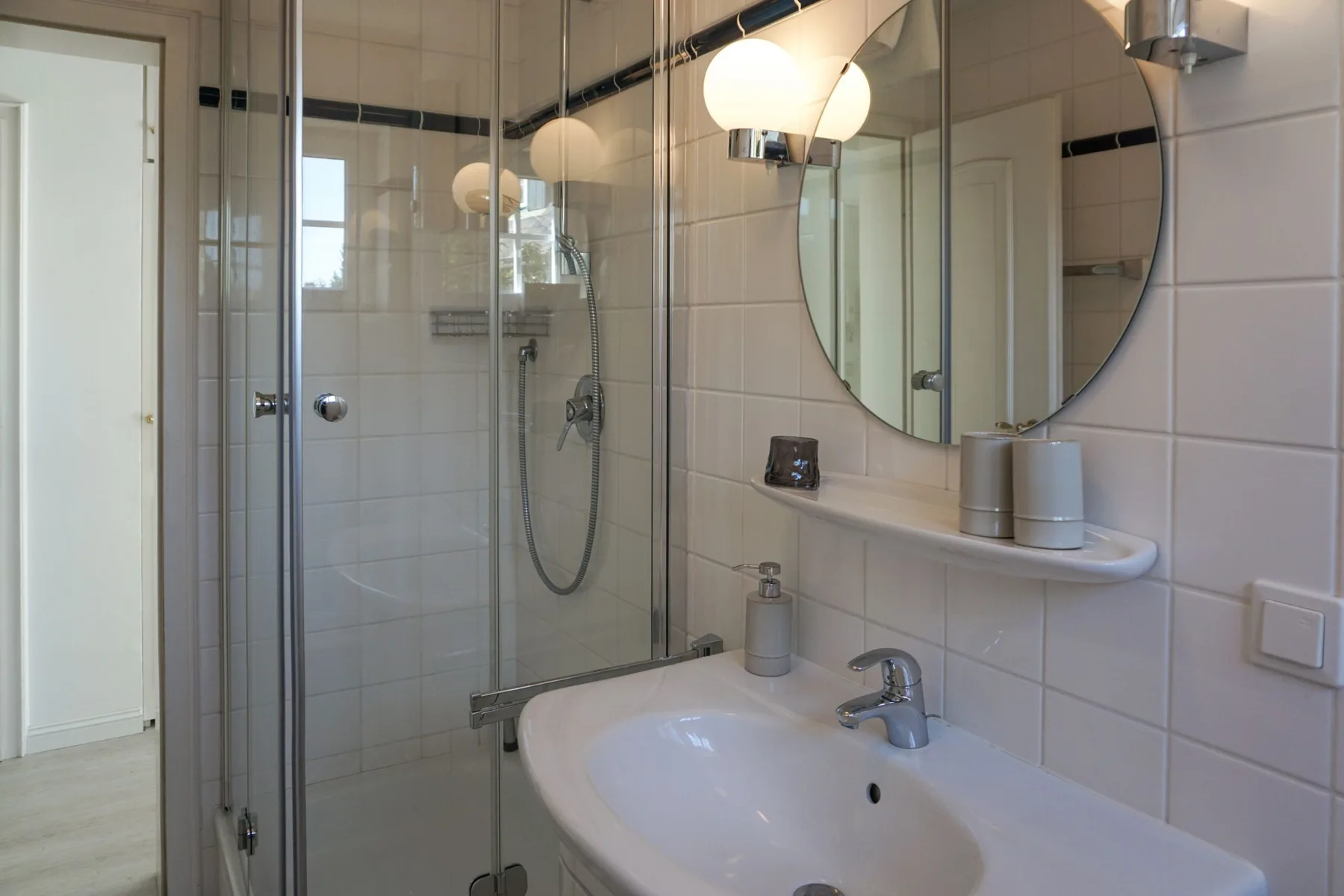 Un baño con azulejos, ducha de vidrio, lavabo y espejo redondo.