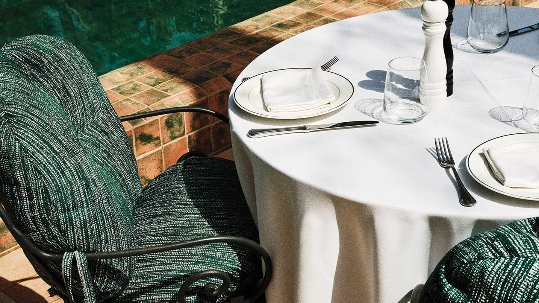 Representative hotel space: A waterside dining table is set with place settings beside a pool.
