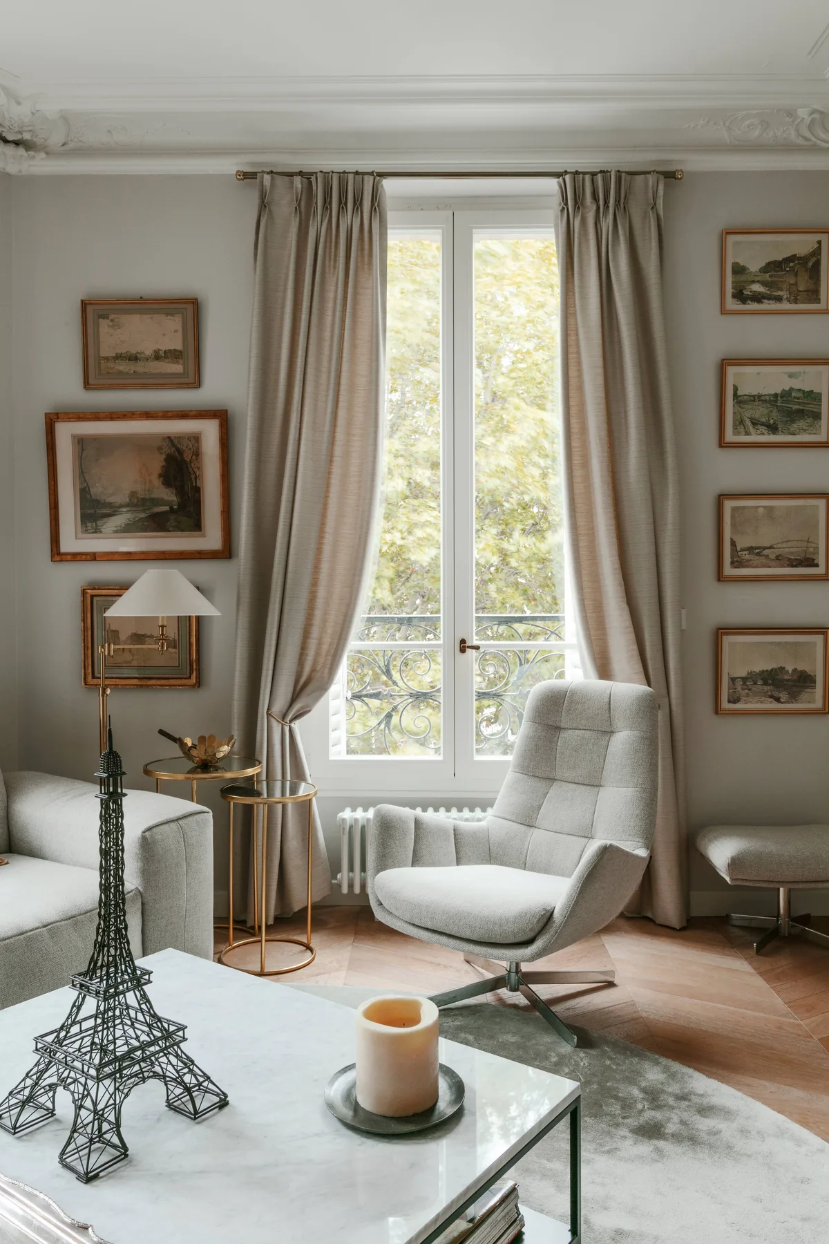 A bright sitting room with a large window, framed artwork, and comfortable seating.