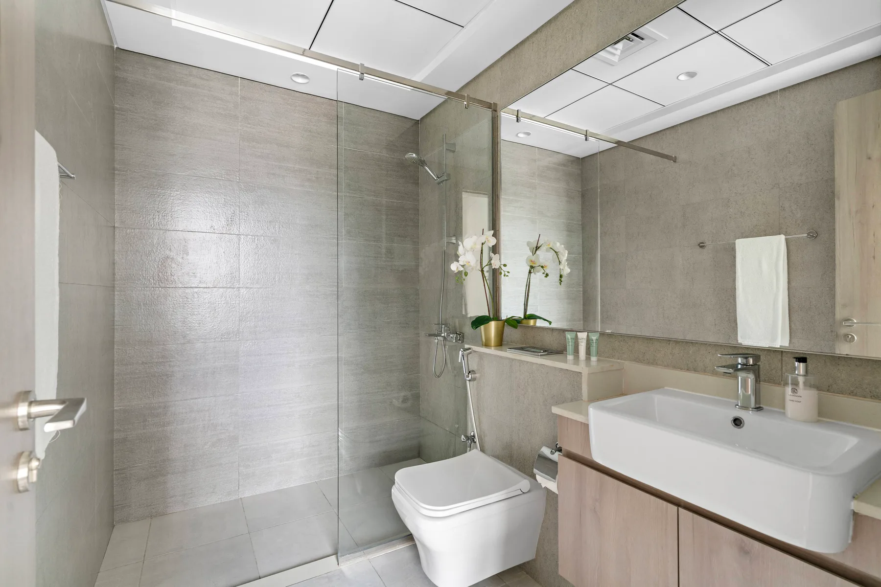 A modern bathroom with a glass shower, toilet, and wide sink.
