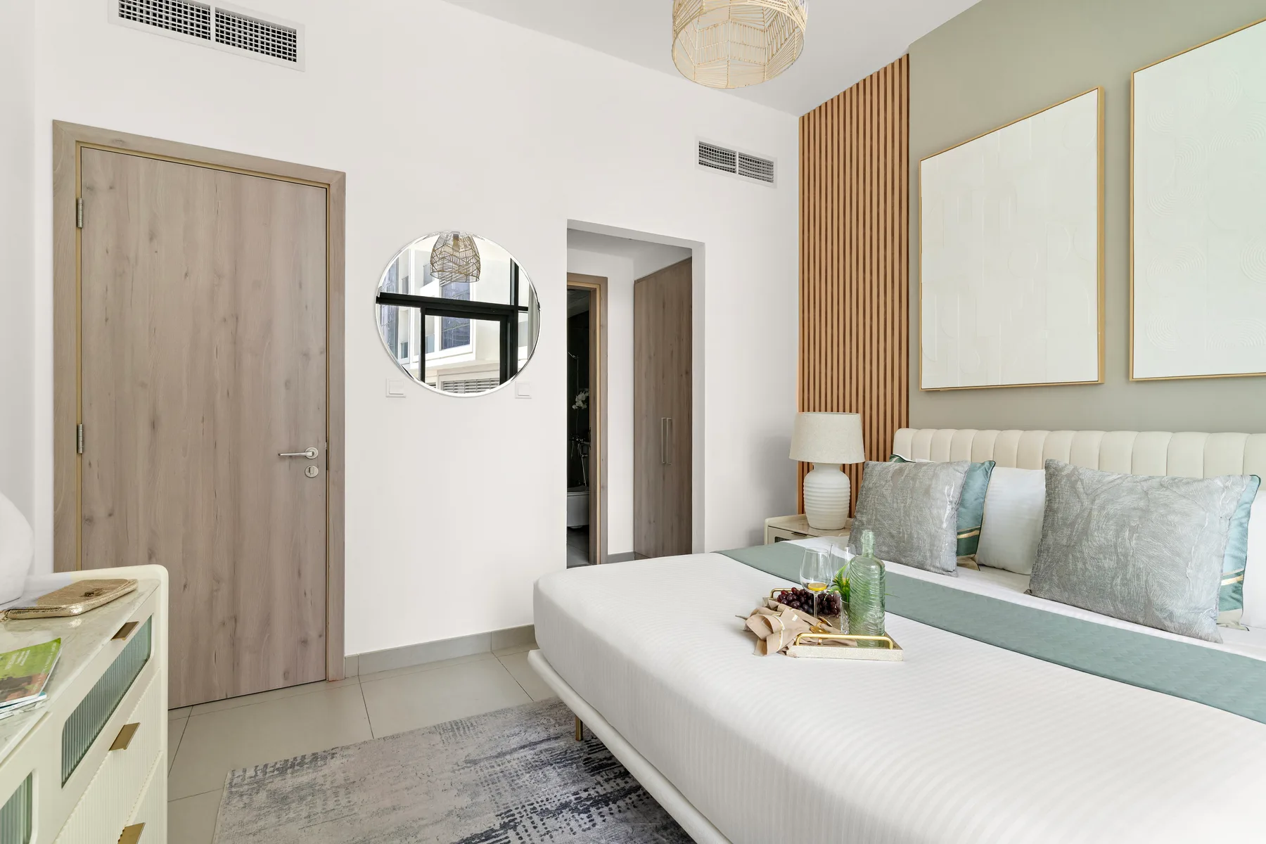 A bright bedroom with a bed, pale bedding, and framed wall art.
