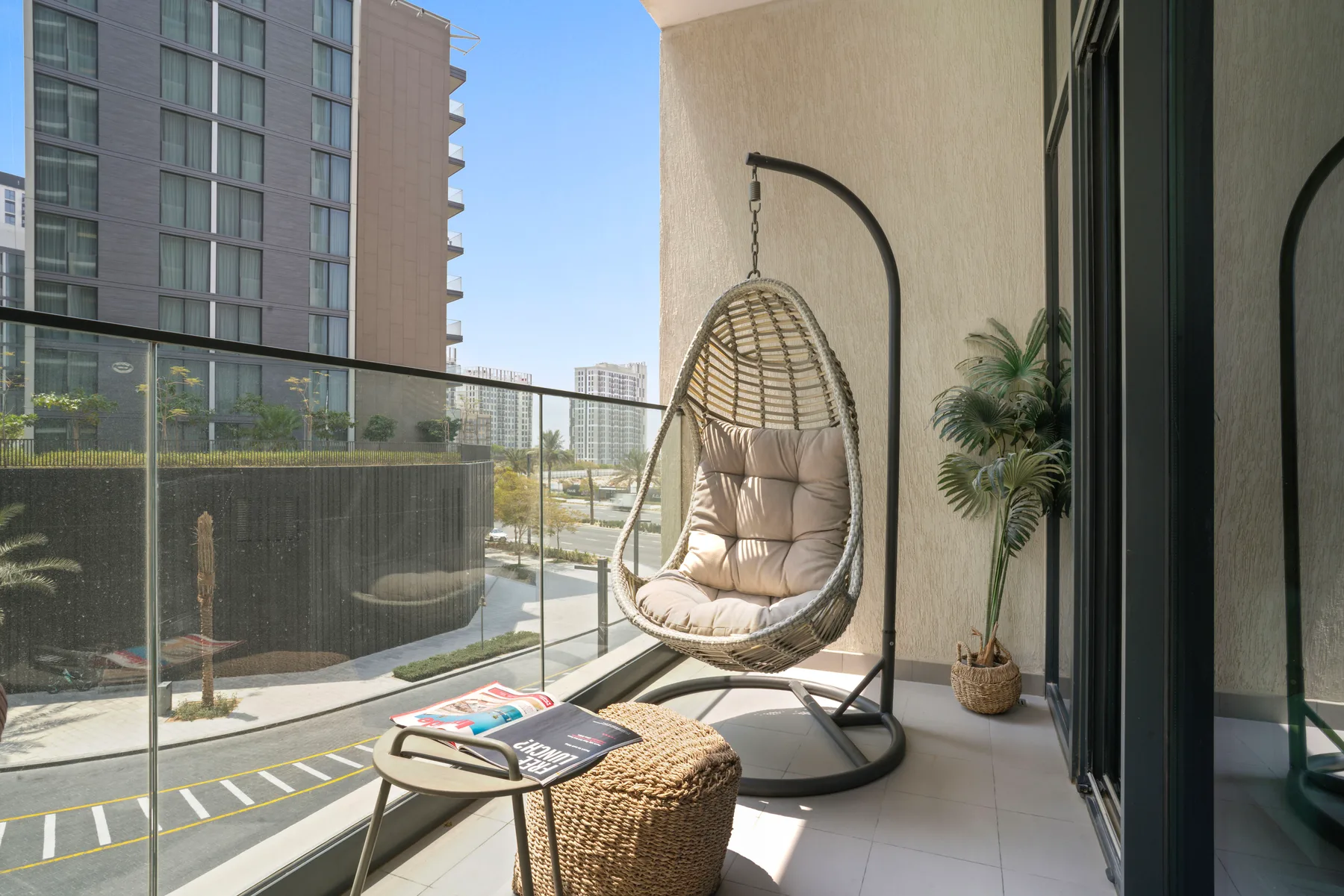 A balcony with a hanging seat, small table, and potted plant.