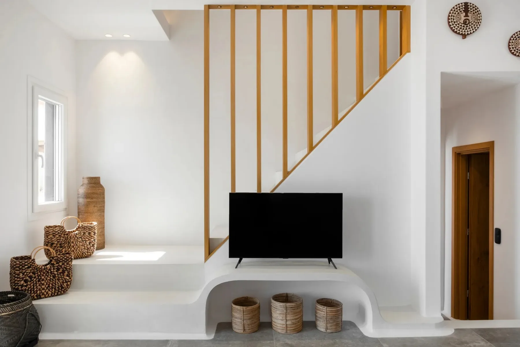 A bright living area with a television beneath a staircase and woven baskets nearby.