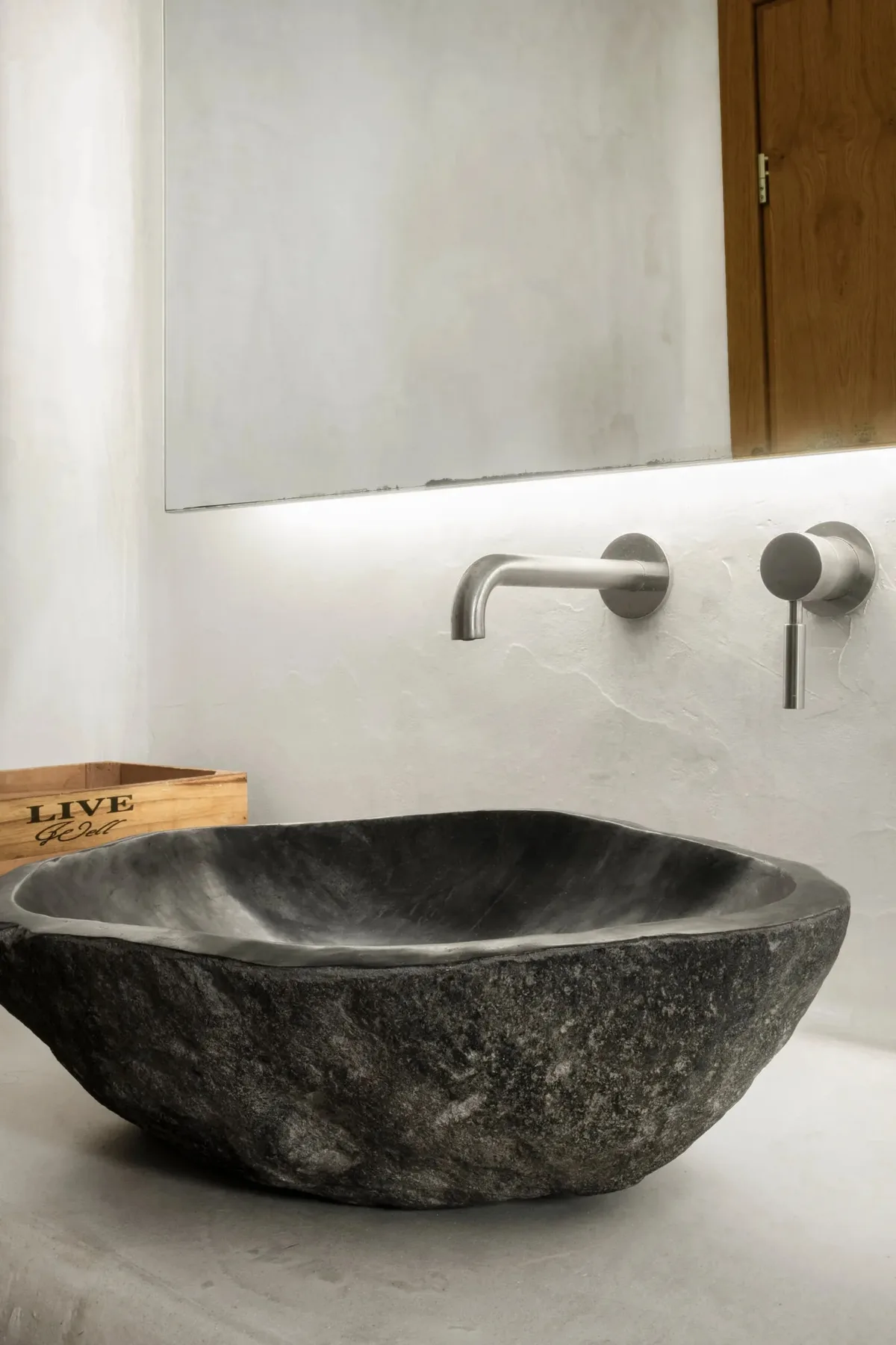 A dark stone vessel sink sits beneath a wall-mounted faucet in a bathroom.