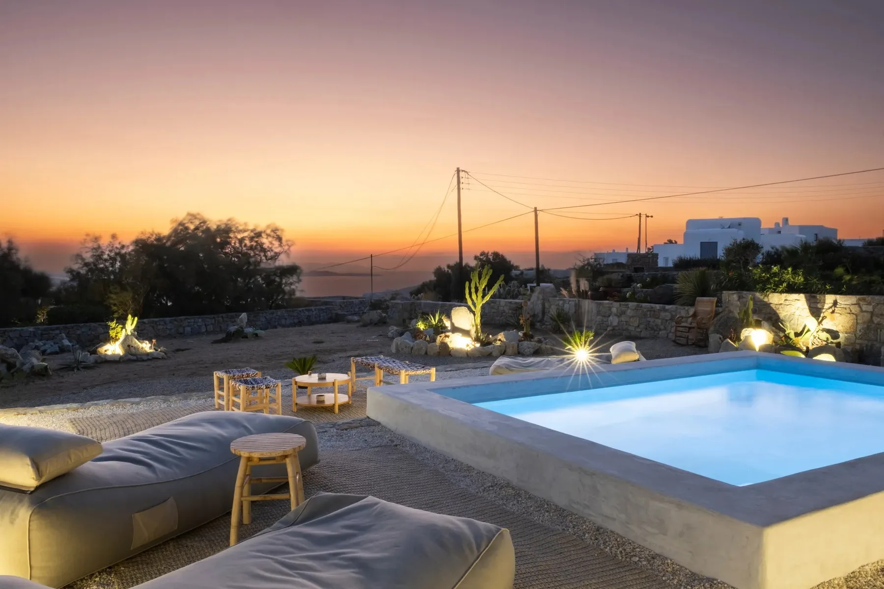 An outdoor pool and seating area are lit beside a stone terrace at sunset.