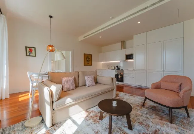 A bright living room with a sofa, armchair, and open kitchen.