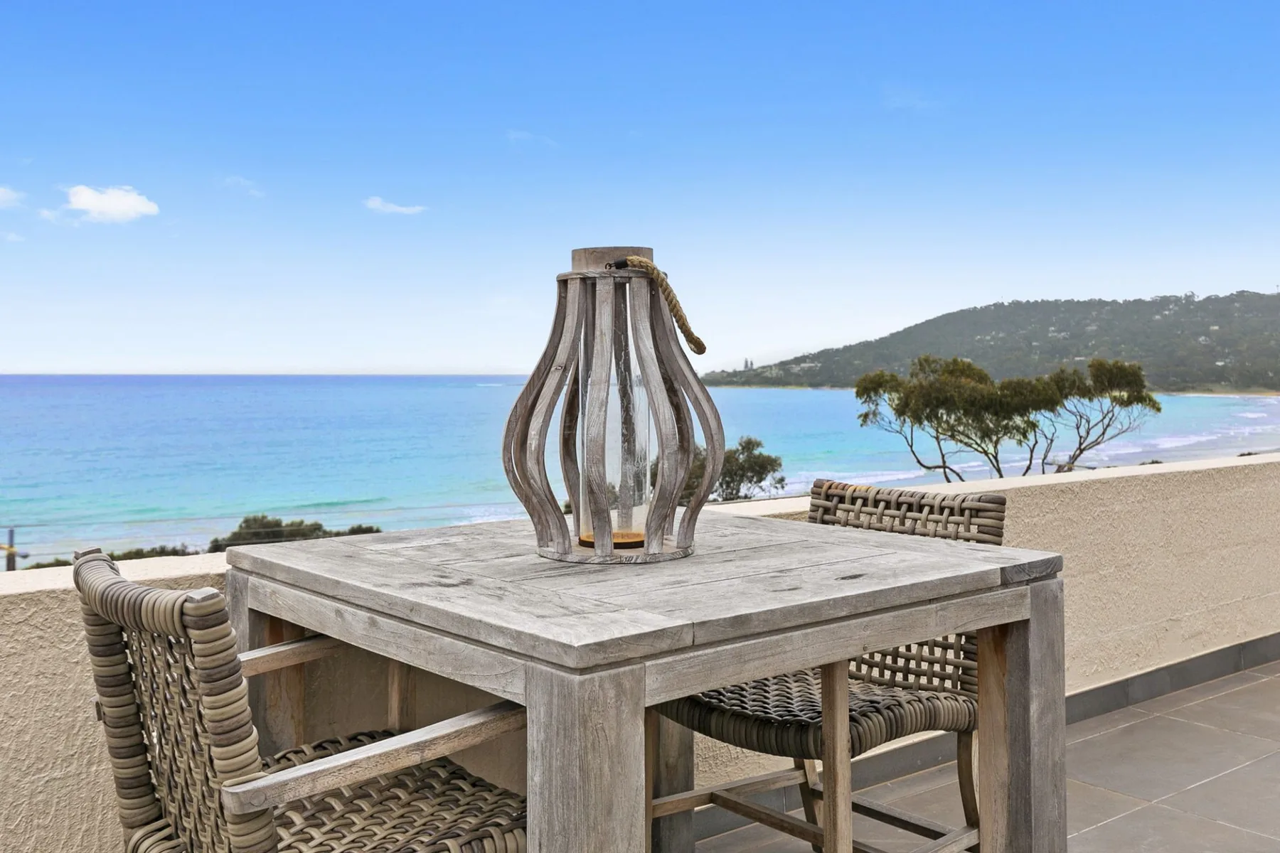 Una mesa de comedor en el patio con asientos tejidos da a una playa de arena y aguas azules.