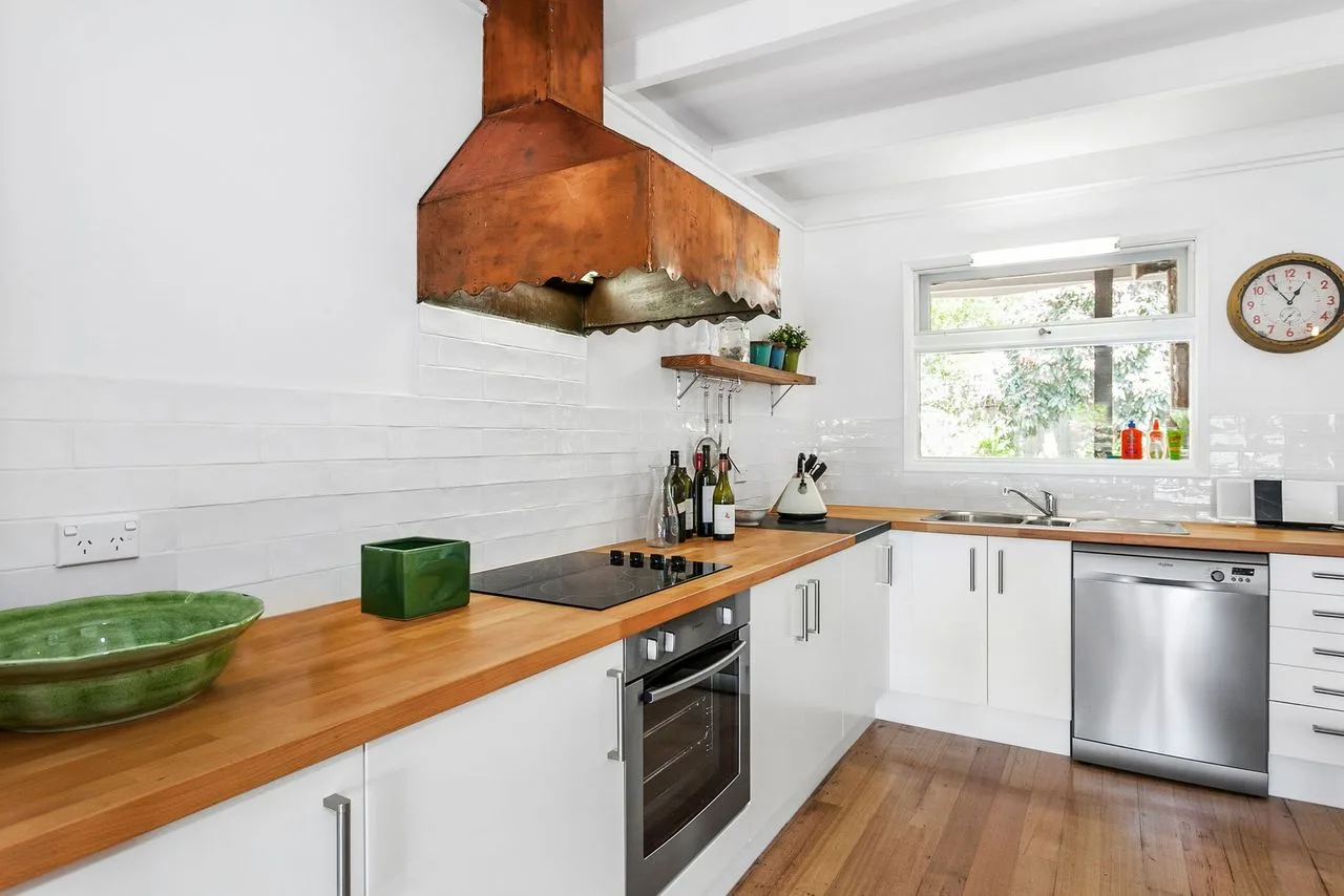 Una cocina luminosa con encimeras de madera, gabinetes blancos y un lavavajillas de acero inoxidable.