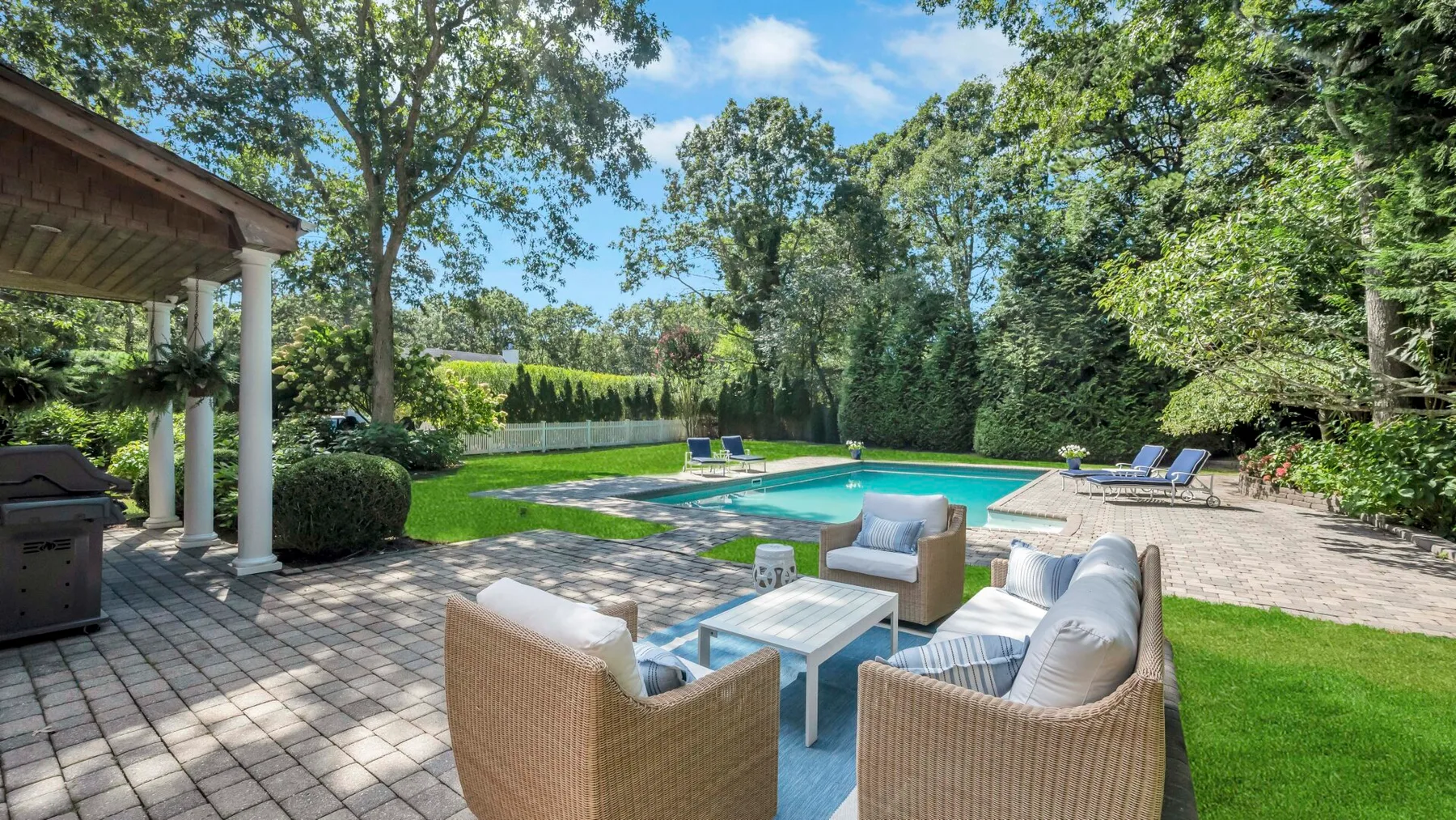 Un patio junto a una piscina al aire libre, con asientos de mimbre.