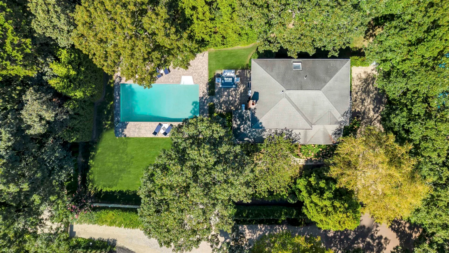Una vista aérea muestra una casa junto a una piscina, rodeada de árboles.