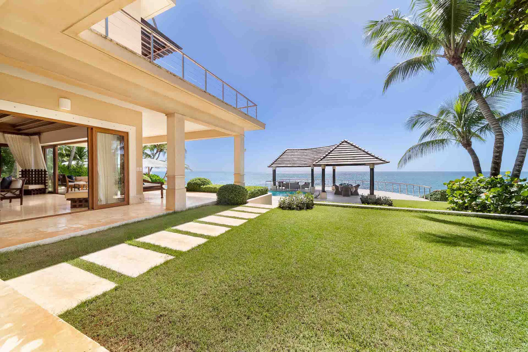A modern house opens onto a lawn with a shaded pavilion beside the sea.