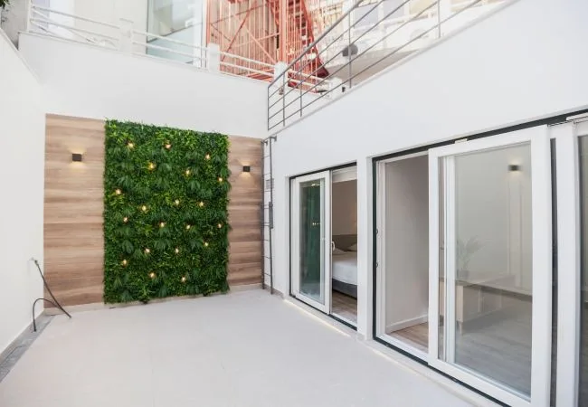 A bright indoor courtyard with a leafy green wall beside sliding glass doors.