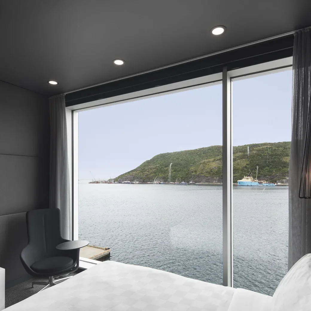 Representative hotel space: A bedroom with a large window overlooking the water and a green hillside.